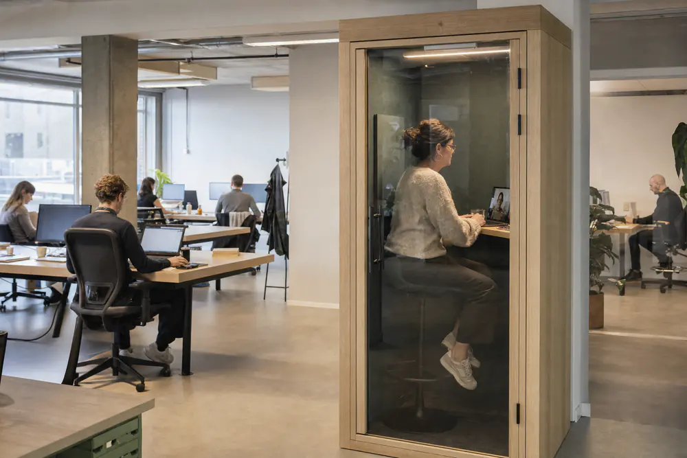 Belcel met glazen deur in een open kantoor, binnen een medewerker in een videogesprek