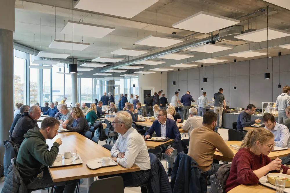 Bedrijfsrestaurant met plafondeilanden en een wand van grijze akoestische panelen