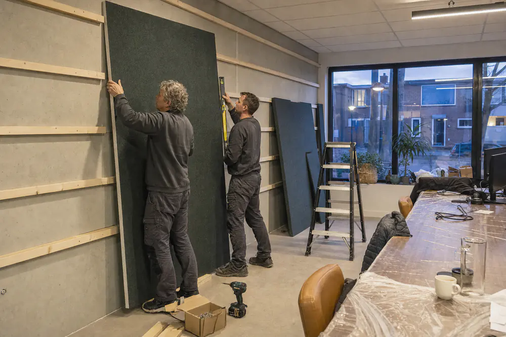 Monteur hangt een plafondeiland op vanaf een rolsteiger in een leeg kantoor