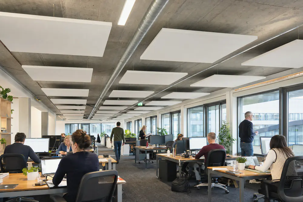 Witte plafondeilanden aan staaldraden onder een betonplafond boven een open kantoor