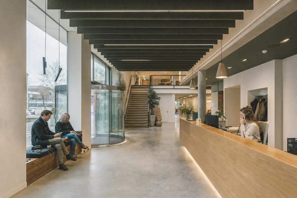Receptie van een kantoorgebouw met groene vilten baffles aan het hoge plafond